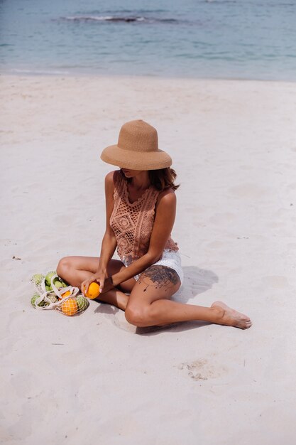 Joven bastante caucásica mujer en forma bronceada en ropa de punto y sombrero en la playa