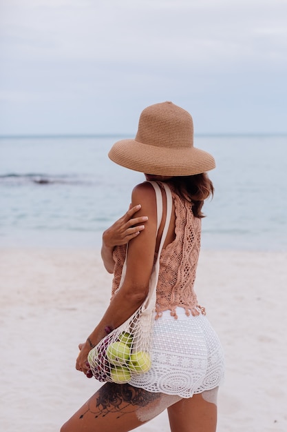 Joven bastante caucásica mujer en forma bronceada en ropa de punto y sombrero en la playa