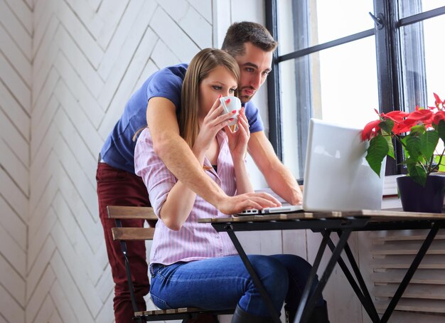 Una joven bebe café y un hombre que trabaja con una laptop.