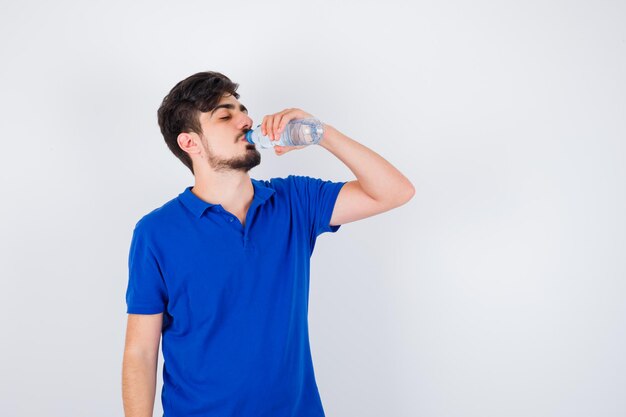 Joven bebiendo agua en camiseta azul y mirando serio