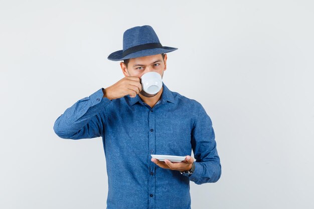 Joven bebiendo café turco en camisa azul, vista frontal del sombrero.