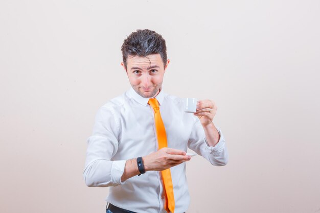 Joven bebiendo café turco con camisa blanca, corbata y mirando alegre