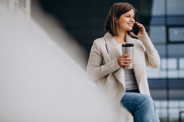 Joven bebiendo café y usando el teléfono fuera de la calle