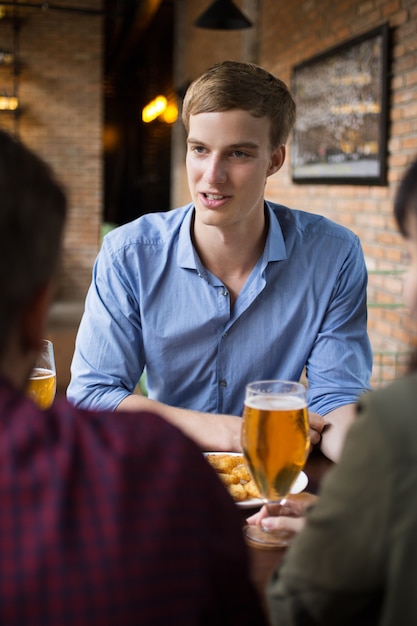 Joven bebiendo cerveza con amigos en el pub