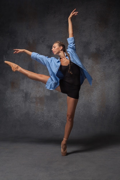 Joven y bella bailarina de estilo moderno con una camisa azul posando sobre un fondo gris de estudio