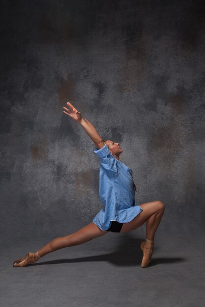 Joven y bella bailarina de estilo moderno con una camisa azul posando sobre fondo gris