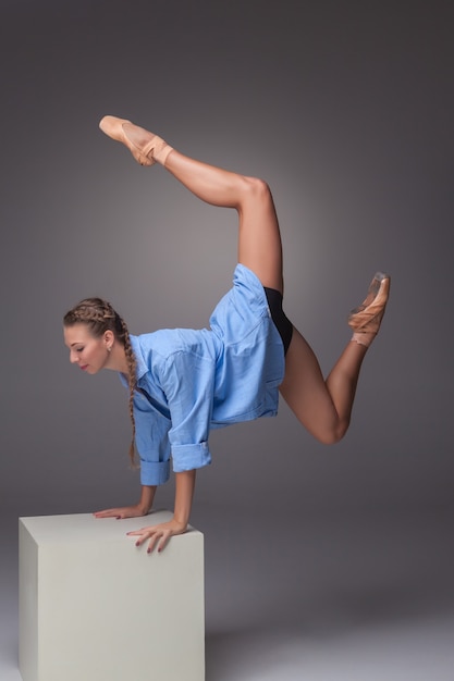 Joven y bella bailarina de estilo moderno posando en un cubo blanco sobre un fondo gris de estudio