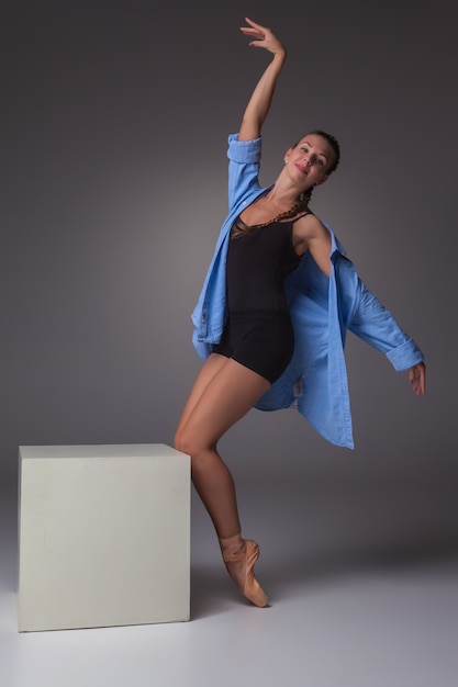 La joven y bella bailarina de estilo moderno posando en un cubo blanco sobre un fondo gris de estudio