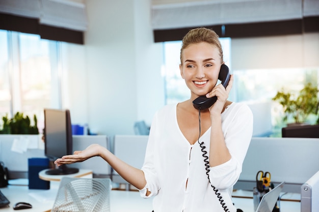 Joven y bella empresaria exitosa sonriendo, hablando por teléfono, sobre la oficina