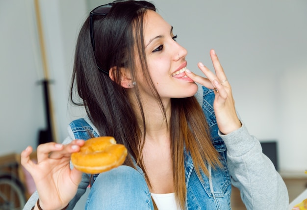 Joven y bella mujer comiendo donas en casa.