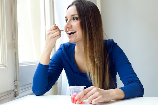 Joven y bella mujer comiendo yogur en casa.