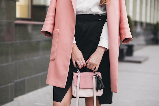 Joven y bella mujer con estilo caminando en la calle, vistiendo abrigo rosa, sosteniendo el bolso, falda negra, traje de moda, tendencia de otoño, accesorios, primer plano de las manos, detalles