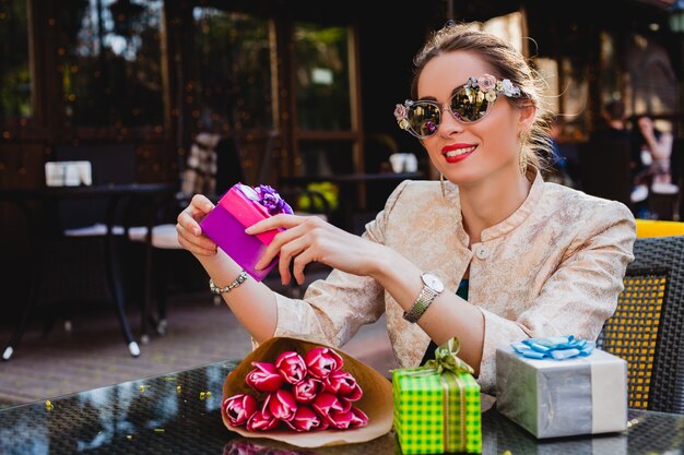 Joven y bella mujer con estilo en gafas de sol de moda sentado en el café