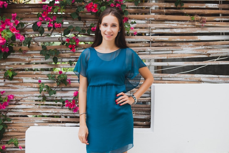 Foto gratuito joven y bella mujer con estilo en vestido azul, tendencia de la moda de verano, vacaciones, jardín, terraza del hotel tropical, sonriendo