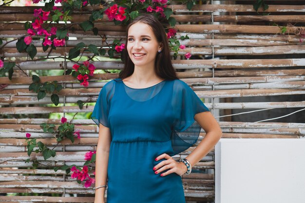 Joven y bella mujer con estilo en vestido azul, tendencia de la moda de verano, vacaciones, jardín, terraza del hotel tropical, sonriendo