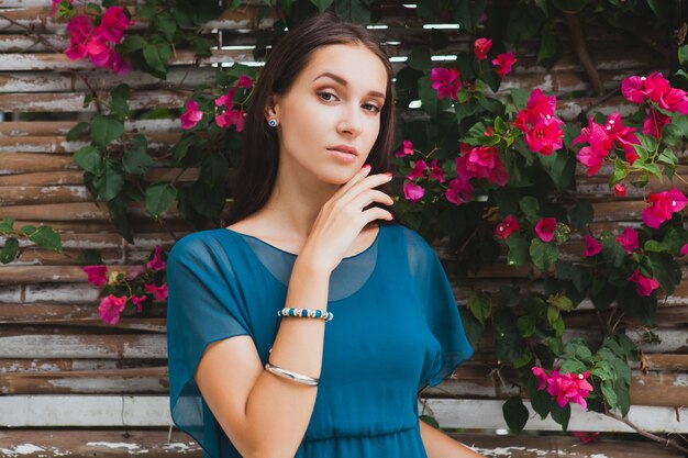 Joven y bella mujer con estilo en vestido azul, tendencia de la moda de verano, vacaciones, jardín, terraza del hotel tropical, sonriendo