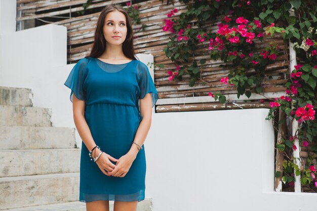 Joven y bella mujer con estilo en vestido azul, tendencia de la moda de verano, vacaciones, jardín, terraza del hotel tropical, sonriendo