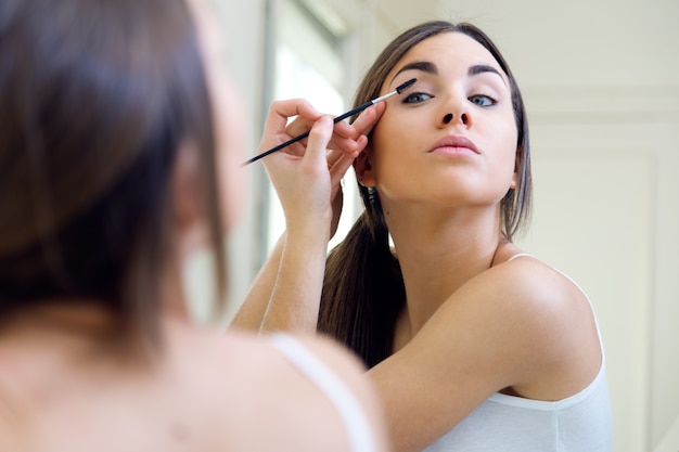 Joven y bella mujer haciendo maquillaje cerca de espejo.