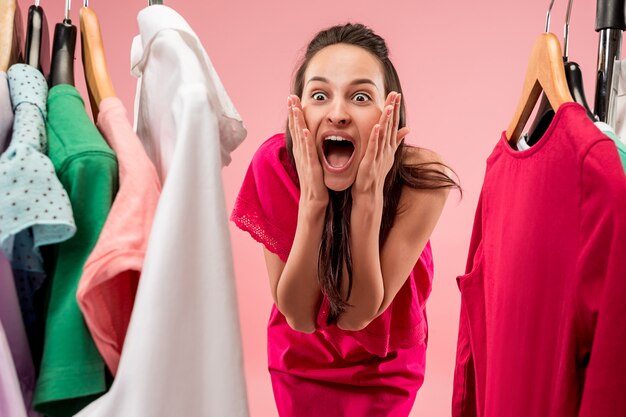 La joven y bella mujer mirando vestidos y probándose mientras elige en la tienda