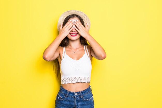 Joven y bella mujer con ojos azules sobre la pared amarilla asomándose en estado de shock cubriendo la cara y los ojos con la mano, mirando a través de los dedos con expresión avergonzada.