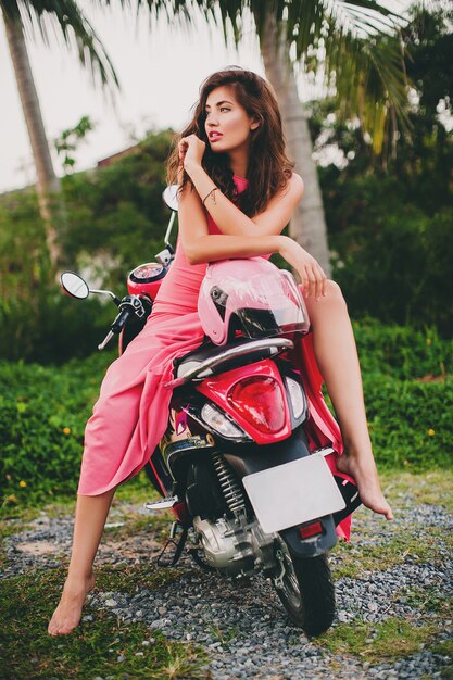 Joven y bella mujer sexy con estilo en vestido rosa en moto scooter