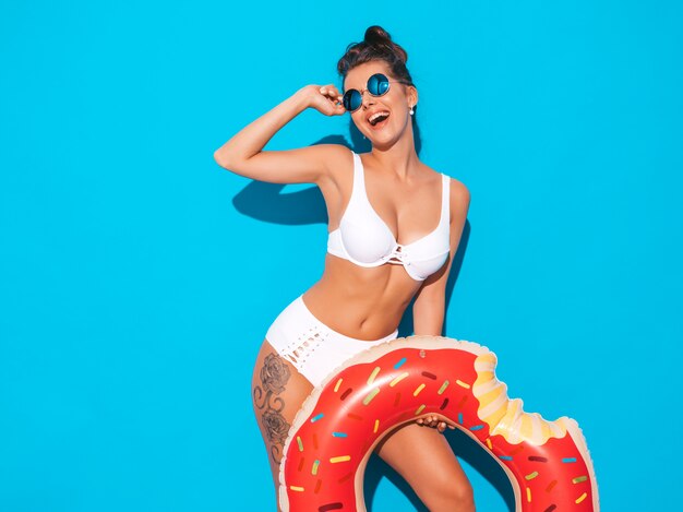 Joven y bella mujer sexy hipster sonriente en gafas de sol. Chica en traje de baño de verano con colchón inflable donut lilo. Mujer positiva volviéndose loca. Modelo divertido