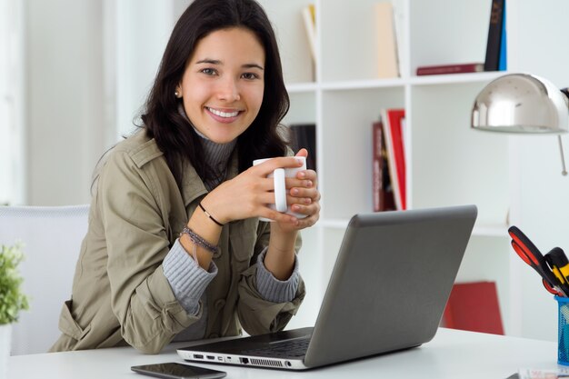 Joven y bella mujer usando su computadora portátil en casa.