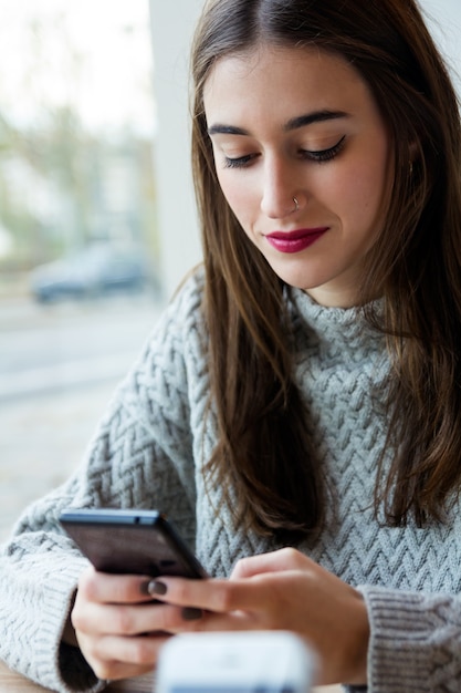 Joven y bella mujer utilizando su teléfono móvil en el café.