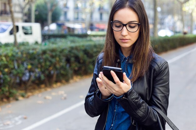 Joven y bella mujer utilizando su teléfono móvil en la calle.