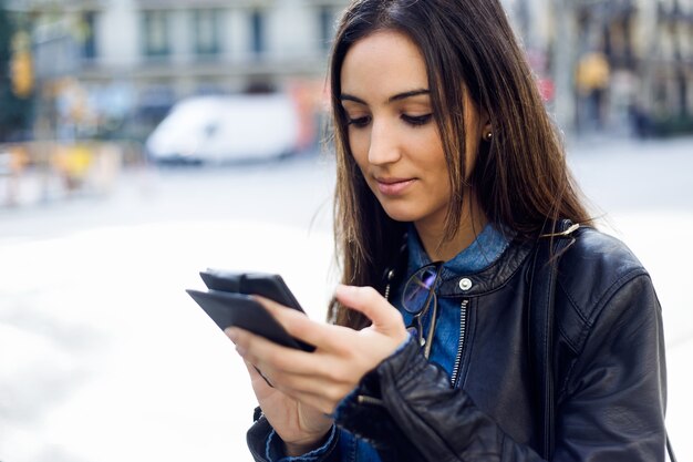 Joven y bella mujer utilizando su teléfono móvil en la calle.