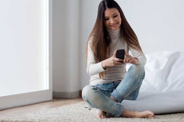 Joven y bella mujer utilizando su teléfono móvil en casa.