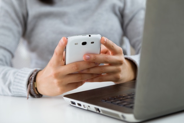 Joven y bella mujer utilizando su teléfono móvil en casa.