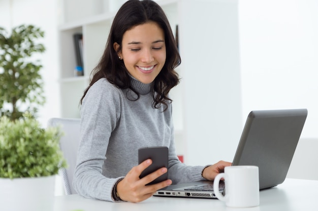 Joven y bella mujer utilizando su teléfono móvil en casa.