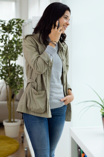 Joven y bella mujer utilizando su teléfono móvil en casa.