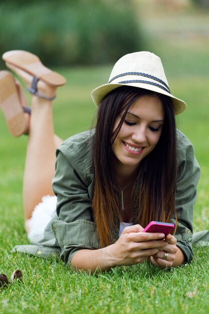 Joven y bella mujer utilizando su teléfono móvil en el parque.