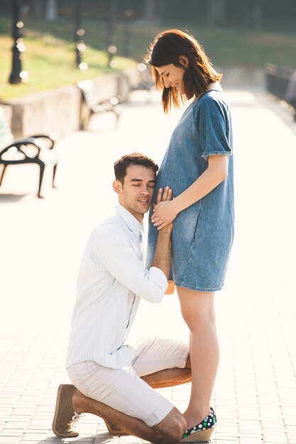 Joven besando el vientre de su esposa embarazada mientras está de pie