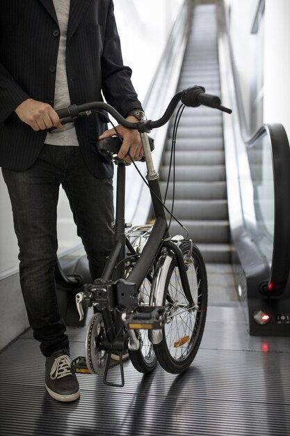 Joven con bicicleta plegable en escalera mecánica