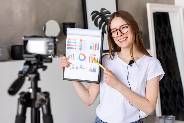 Joven blogger grabando con cámara profesional con portapapeles con gráficos