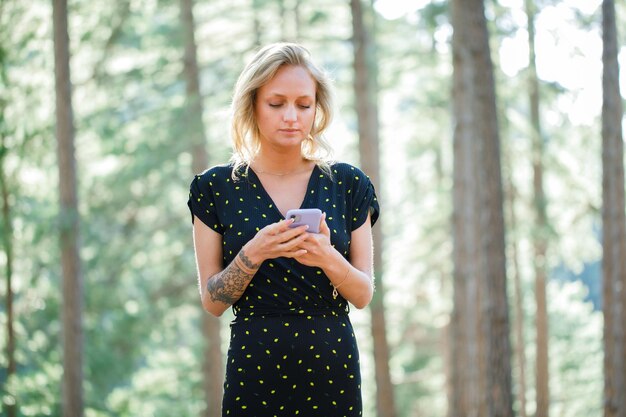 La joven bloguera sostiene el móvil con las dos manos y mira el móvil en el fondo de la naturaleza
