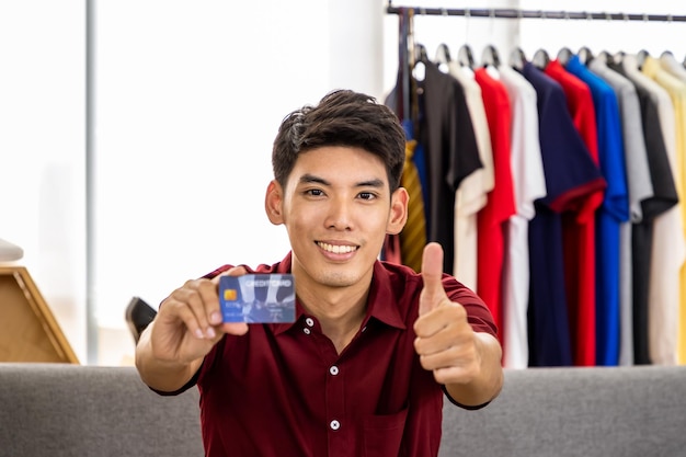 Joven bloguero comerciante en línea asiático masculino video en vivo para vender con tarjeta de crédito con el pulgar hacia arriba mirando a la cámara Concepto de pago y compras en línea de influencer de redes sociales