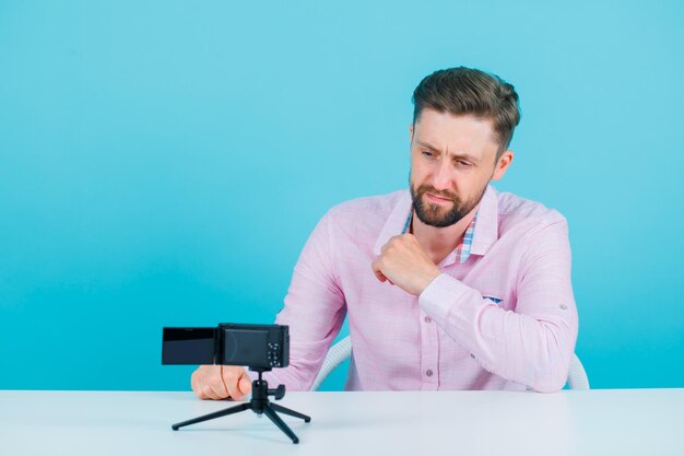 El joven bloguero está posando para su mini cámara con fondo azul.