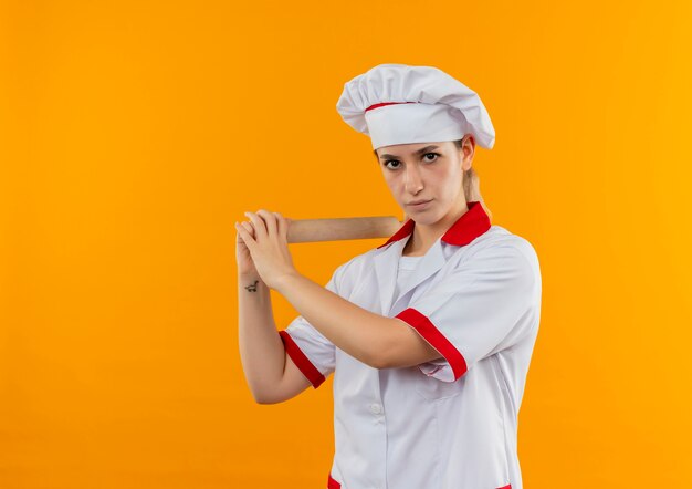 Joven bonita cocinera en uniforme de chef con rodillo comenzando a batir