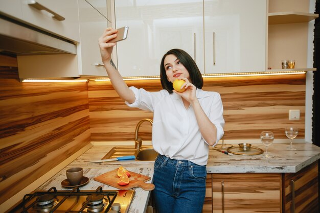 joven y bonita morena de pie en la cocina con teléfono