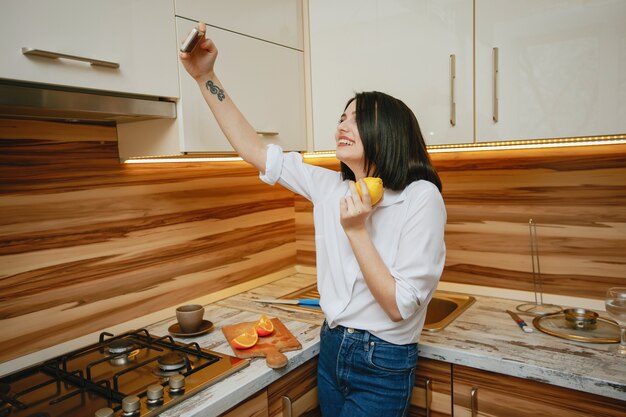 joven y bonita morena de pie en la cocina con teléfono