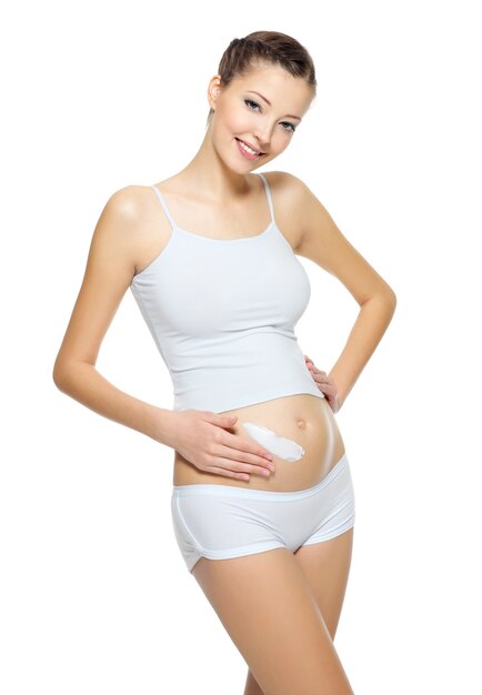 Joven bonita a mujer embarazada aplicando crema cosmética en el estómago - aislado en blanco