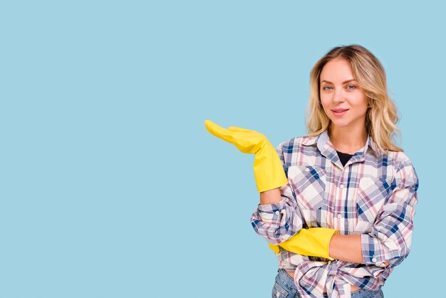 Joven bonita presentable con guantes amarillos de pie delante de la superficie azul