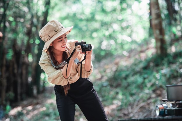 Joven bonita tomando una foto con una cámara digital, mira la foto y sonríe con felicidad mientras acampa en el bosque Grupo de mujeres jóvenes asiáticas viajan para acampar al aire libre