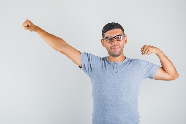 Joven bostezando brazos y sonriendo en camiseta gris, gafas y mirando relajado