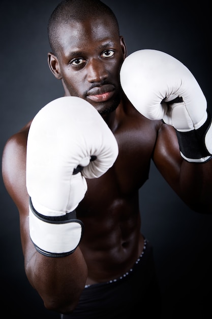 Joven boxeador atlético con guantes en fondo negro.
