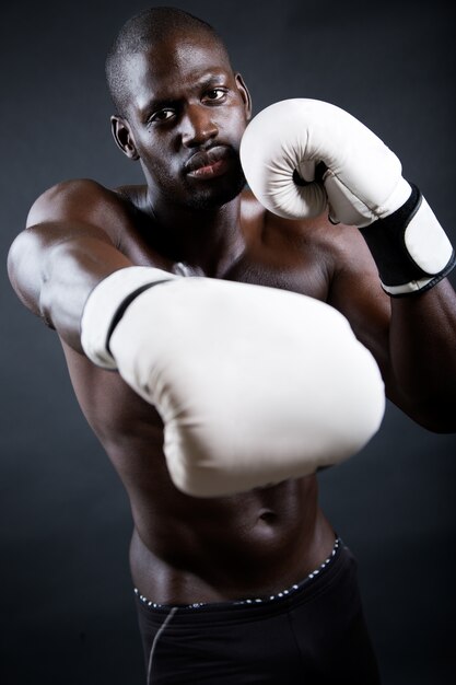 Joven boxeador atlético con guantes en fondo negro.